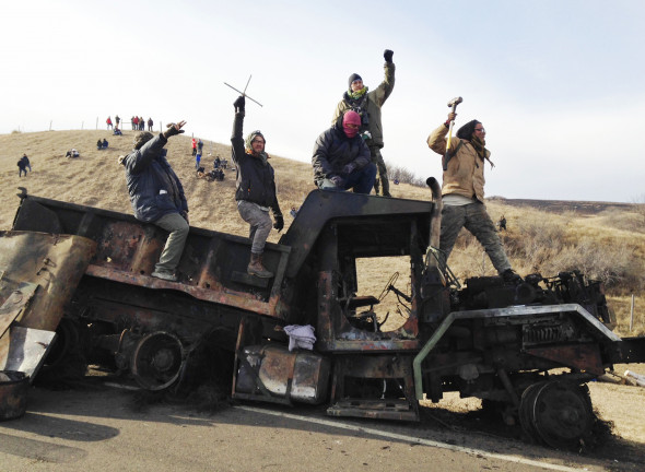 Protesters demonstrating against the Dakota Access oil pipeline stand on a burned-out truck near Cannon Ball, N.D., which they removed a day earlier from a long-closed bridge on a state highway near their camp, Nov. 21, 2016. Photo: James MacPherson/AP